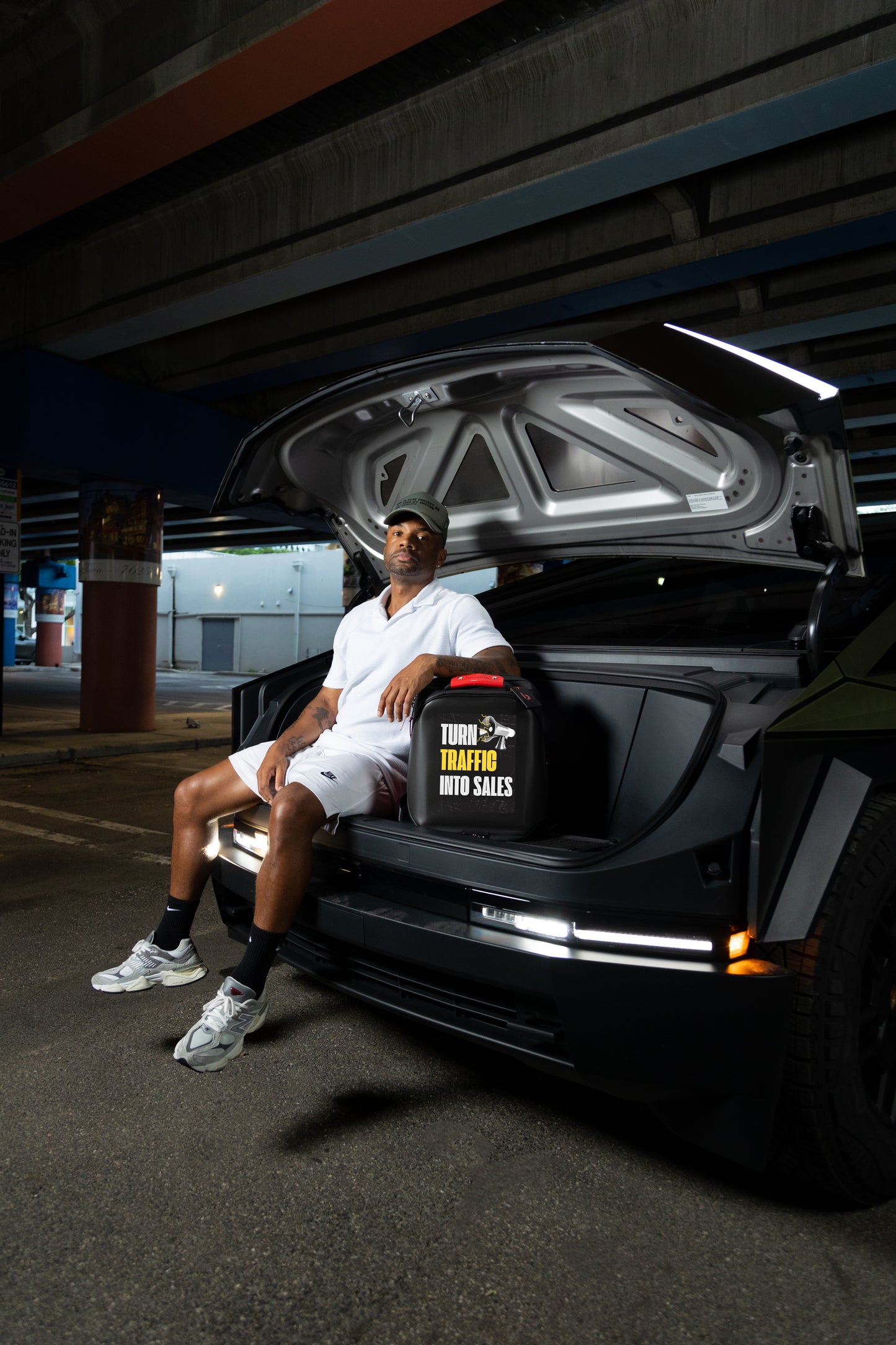 Man sitting inside an open car trunk with a red eye led billboard bag labeled 'Tough Traffic Now Sales' 